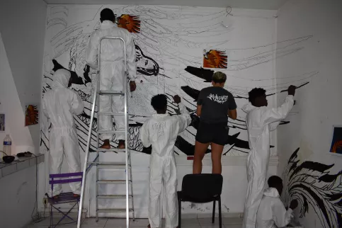 Groupe de jeunes en tenus de peintre qui peignent une fresque murale qui représente un Phoenix 